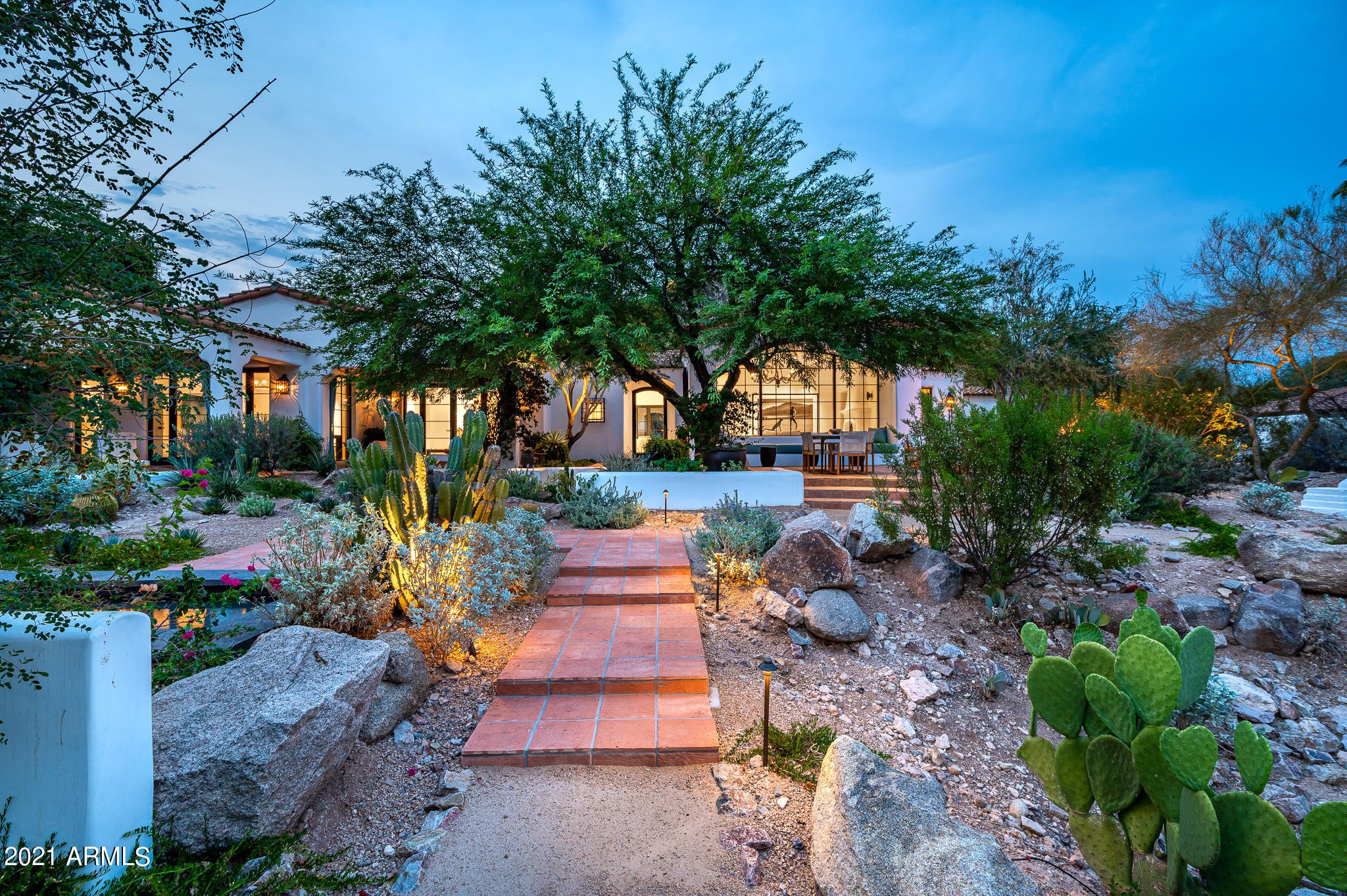 Desert luxury home with stone steps and native landscaping against a mountain backdrop at dusk