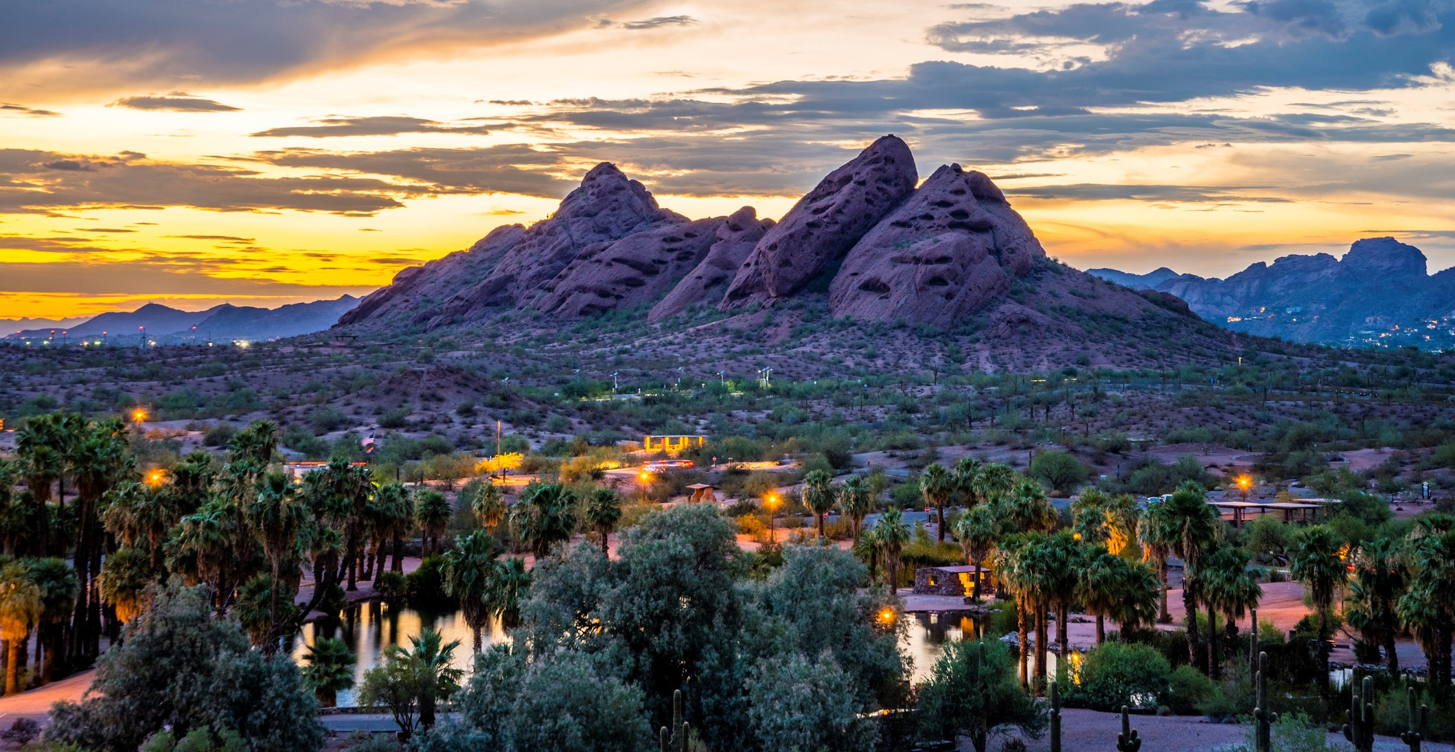 Red desert buttes and palm trees reflected in water at sunset in the Phoenix area